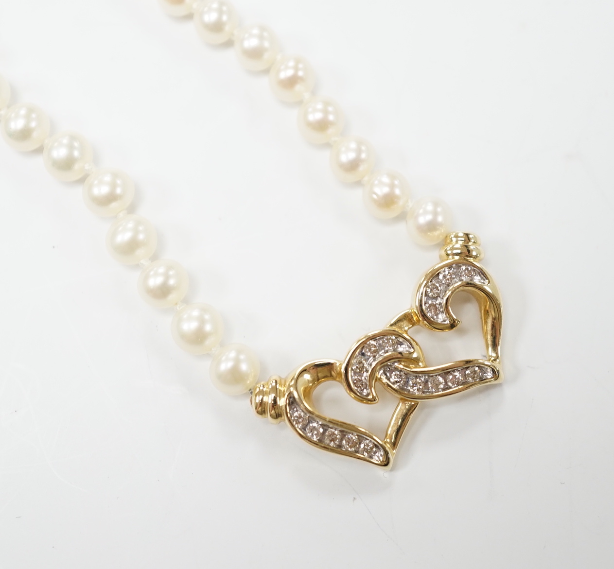 A modern single strand cultured pearl necklace, with central diamond chip set 14k yellow metal twin hearts motif, 42cm, gross weight 15.2 grams.